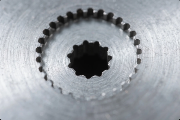 This image captures a macro view of a precision-machined metal part, focusing on the inner gear-like teeth surrounding a central hole. The teeth are evenly spaced and clearly defined, highlighting the high level of accuracy in the manufacturing process. The surrounding metal surface displays fine machining marks and a polished finish, emphasizing the component's quality and attention to detail. This type of part is typically used in mechanical transmission, couplings, or gear assemblies, representing advanced manufacturing and strict quality control standards.