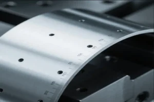 Close-up view of a curved metal sheet with precise measuring marks, showing detailed dimensions and manufacturing accuracy.