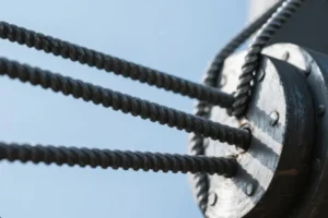 Close-up of steel cables twisted together, attached to a heavy-duty metal fixture, showcasing the strength and precision of industrial cable assemblies.