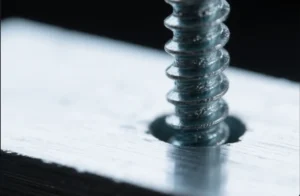 Close-up of a self-tapping screw threaded into a metal plate, showing fastener engagement and thread profile.