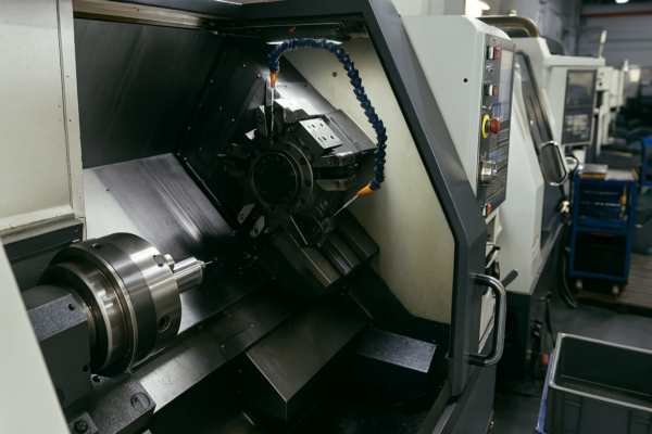 This high-resolution image captures a CNC turning center inside the Prime workshop. The focus is on the machine’s spindle and tool turret, with a mounted metal workpiece and visible coolant nozzles. The background shows additional CNC equipment and a functional, organized workspace, demonstrating precision machining in an industrial setting.