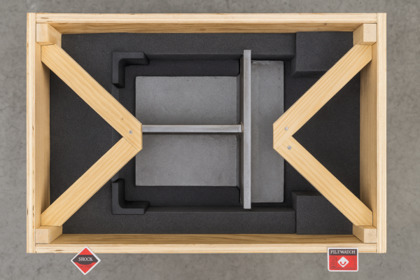 Packaging layout for custom metal welding parts showing an open wooden crate with bracing, foam padding, corner guards, and external shock/tilt indicators.