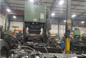Wide view of an industrial metal stamping press in a production workshop with stamped scrap and tooling in the foreground.