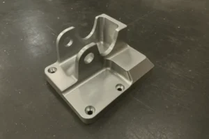 Precision CNC machined aluminum bracket with mounting holes and smooth milled surfaces on a workbench