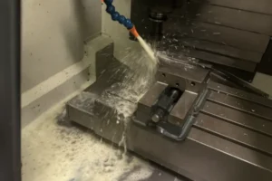 CNC machined aluminum bracket with a circular pocket and bolt holes, placed on a machine table after milling.