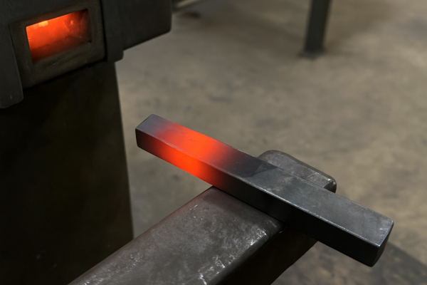 Heat treatment process showing a steel bar heated to red-hot in a furnace, preparing metal parts for improved strength and hardness.
