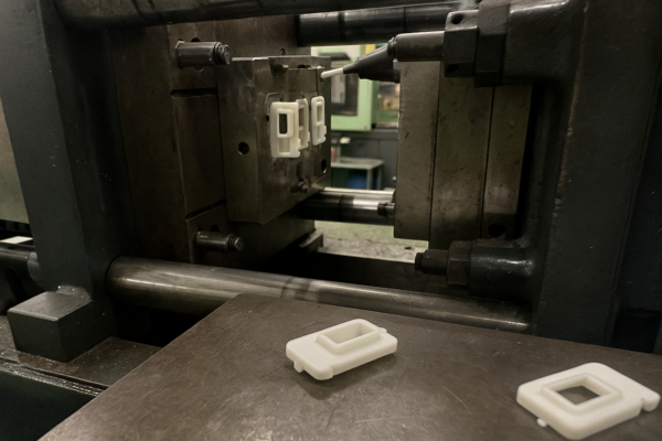 Injection molding machine producing custom white plastic components, with molded parts placed on the press table during OEM production.