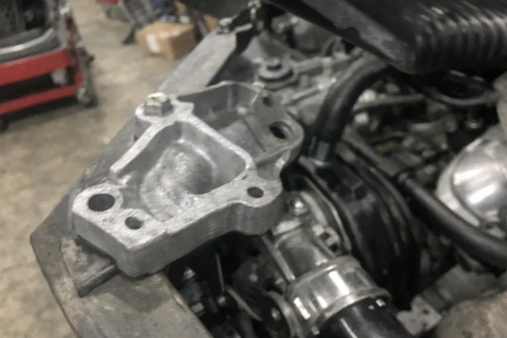 Custom-made cast aluminum automotive brackets are installed on engine components in the workshop.