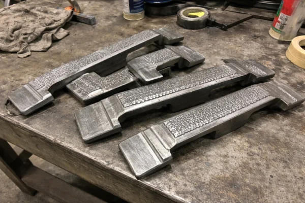 Custom wear-resistant grate bars with hardfacing overlay laid out on a workshop workbench for inspection