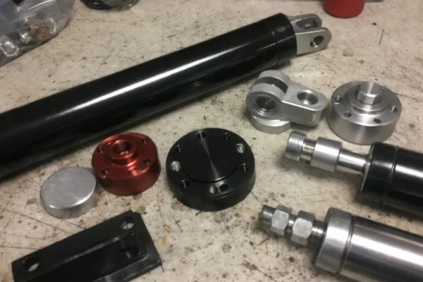Custom hydraulic and pneumatic cylinder components on a workbench, coated cylinder tube with assembly-ready end caps and fittings