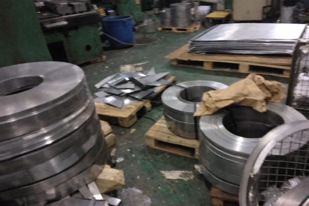 Custom metal stamping material preparation with steel coils and stacked sheet blanks on pallets in a factory workshop
