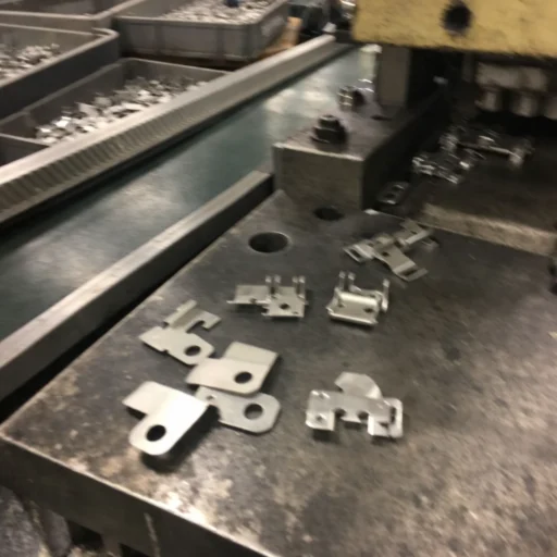 Custom metal stamping parts on a press table beside a conveyor line, showing precision stamped brackets and clips