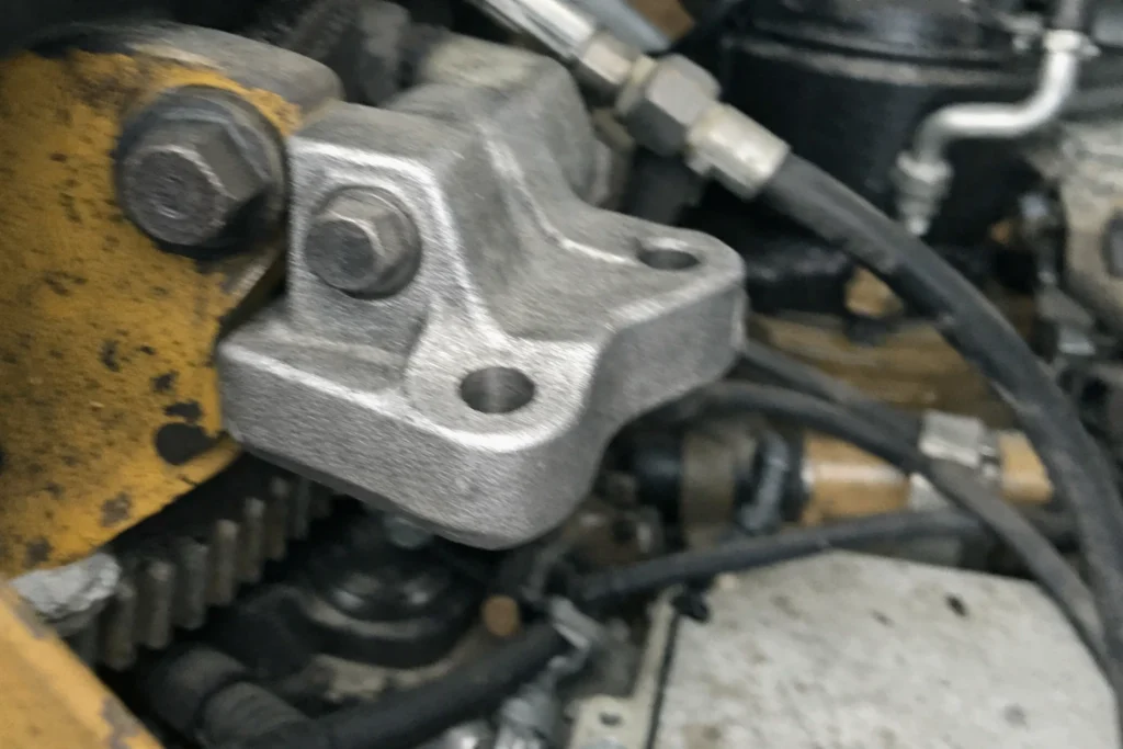 Custom metal casting bracket mounted on industrial machinery, close-up of a rough-finish cast component with bolt holes