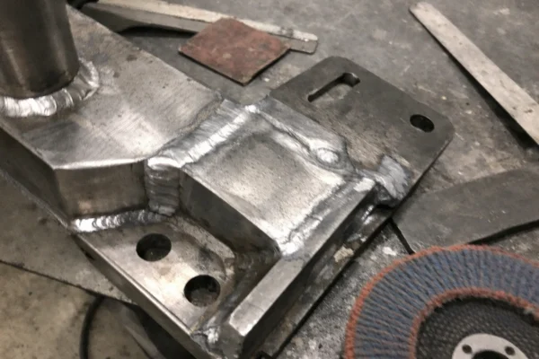 Custom welded metal part with ground and blended weld seam before coating, on a workshop bench