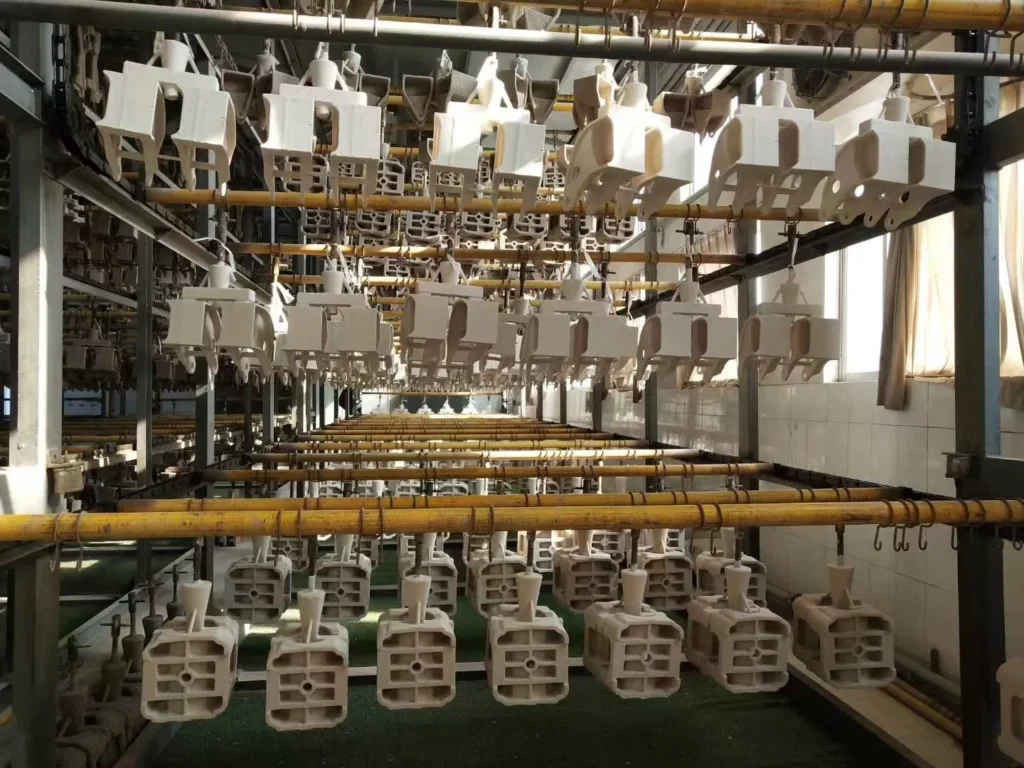 Investment casting ceramic shell molds hanging on a drying line in a foundry, showing multiple shell assemblies prepared before dewaxing and metal pouring.